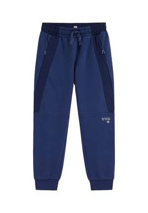 Pantalon de jogging bleu marine avec taille élastique, poches latérales zippées, cordon de serrage, chevilles côtelées et petit texte blanc sur la jambe droite.
