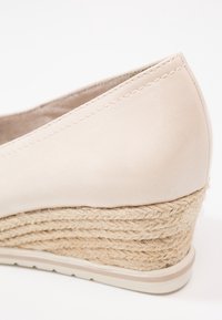Chaussure compensée beige avec dessus lisse et détail de talon en corde tressée, avec une semelle en caoutchouc texturée pour l'adhérence.
