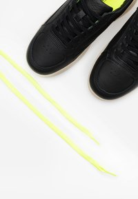 Baskets en cuir noir avec surface texturée, dotées de lacets et semelles intérieures vert fluo, à bout rond, et semelles en caoutchouc beige.