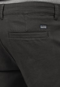 Sorte denim bukser med en baglomme med en vandret klap. En lille "BLEND" mærkat er fastgjort nær lommen. Glat tekstur og skræddersyet pasform.