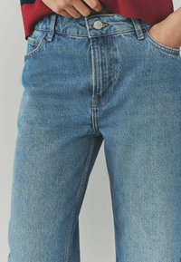 Jeans in denim azzurro chiaro con taglio dritto, dotati di chiusura a bottone, tasche standard e motivi di cucitura ben visibili.