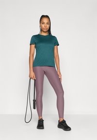 Tyrkis sports-t-skjorte, korte ermer, og grå-lilla leggings. Sorte joggesko og et hoppetau som tilbehør. Glatte stoffer, tettsittende design.