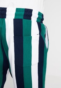 Joggers rayés présentant des rayures verticales vertes, bleu marine et blanches, réalisés en coton doux avec une ceinture élastique et une seule poche arrière.