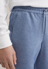 Mėlynos medvilnės ir poliesterio blendinės sportinės kelnės su tekstūruotu audiniu, elastinga juosta ir raišteliu. Turi šonines kišenes ir laisvą siluetą.