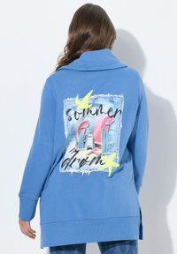 Felpa blu con collo cowl, caratterizzata da un design grafico colorato sul retro, con sedie da spiaggia e accenti gialli.