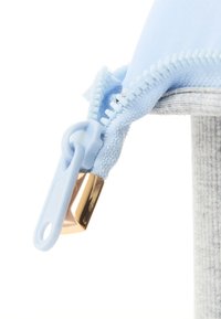 Blått stoff med en gull-accentert glidelås, med en teksturert overflate og kontrasterende grått stoff i nærheten. Nærbilde av glidelåsdetaljen.