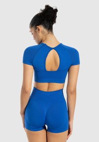 Completo sportivo blu che presenta una maglietta a maniche corte con un'apertura sul retro e pantaloncini a vita alta. Tessuto liscio, design aderente.