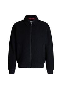 Zwarte wollen bomberjack met een rits voorkant, staande kraag en ribboorden aan de mouwen en onderkant. Voorzien van zijzakken en een voeringdetail in het rood.