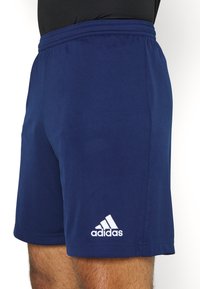 Shorts de sport Adidas bleu marine avec taille élastique portés par une personne, montrant le logo Adidas sur la partie inférieure de la jambe gauche.