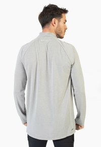 Camisa gris de manga larga con un patrón texturizado, dobladillo redondeado y mangas raglán. Presenta un logo en la parte posterior y un diseño ajustado.