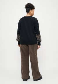 Μαύρη φούτερ με_patterned_μανίκια, συνοδευόμενη από καφέ κοτλέ παντελόνι και χοντρές μαύρες μπότες, βλέπεται από πίσω.