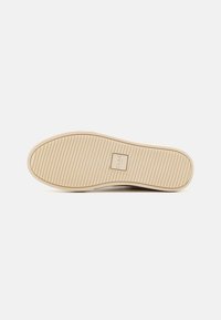Semelle d'une sneaker présentant une surface en caoutchouc texturé couleur crème avec des rainures horizontales et une zone centrale avec le logo "CLAE."