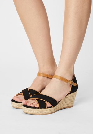 Schwarze Keilsandalen mit Kreuzriemendesign und braunem Knöchelriemen. Sie verfügen über eine strukturierte Espadrillesohle und sind offen an der Zehe.