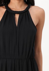 Vestido preto sem mangas com decote trançado, apresentando um recorte em forma de olho-chave e cintura franzida, feito de tecido leve.