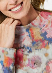 Mehrfarbiger Pullover mit hohem Kragen, weicher Textur und einem lebhaften Blumenmuster in verschiedenen Rosa-, Blau- und Beigetönen.