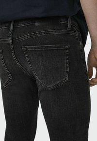 Svart denimjeans med en tettsittende design, subtil tekstur og to baklommer med et unikt broderimønster, merkeetikett synlig.