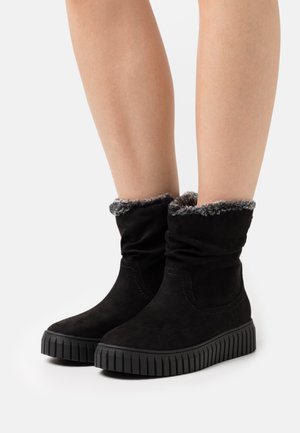 Schwarze Wildleder-Stiefeletten mit einem lässigen Design, ausgestattet mit einem weichen grauen Kunstfellbund und einer flachen Gummisohle mit gerippter Textur.