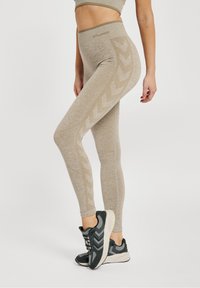 Beżowe legginsy z wysokim stanem z teksturowanym wzorem w chevrony po bokach, wykonane z miękkiego, elastycznego materiału.