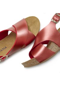Red leather sandals with crisscross straps, a cork footbed, and a silver buckle detail. Flat sole with a smooth texture.