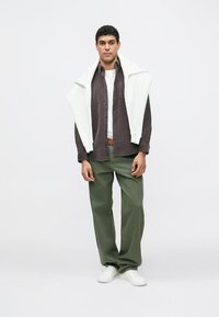 Tumesinine nööpidega särk, valge ringikaelusega T-särk, oliivrohelised püksid ja valged tennised, valge kampsun üle õlgade laotatud.