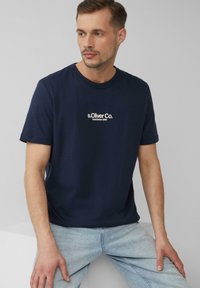 Navyblauwe katoenen T-shirt met korte mouwen, ronde hals, featuring wit "s.Oliver Co." logo op de borst, gecombineerd met lichtblauwe spijkerbroek.