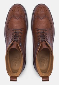 Stivali in pelle marrone con finitura texturizzata, dettagli brogue e lacci, con una fodera interna liscia e tacco rinforzato.