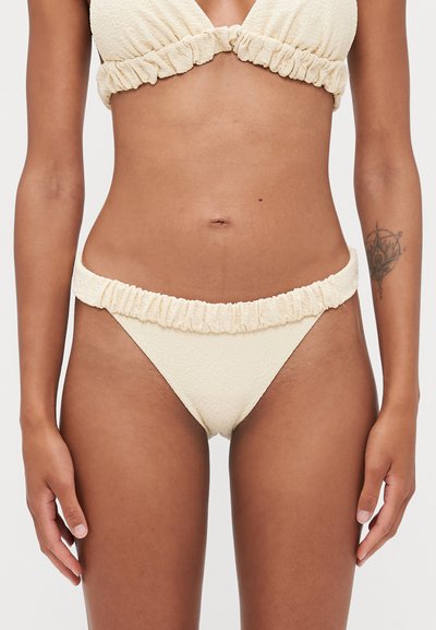 Bikini de couleur crème avec un tissu texturé, des bords froncés sur le haut et le bas, et un design minimaliste avec un bralette triangulaire.