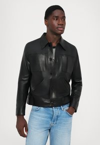 Melna ādas jaka ar pogu aizdari, diviem atloku kabatām un apkakli. Valkāta virs pelēka topa un apvienota ar gaiši ziliem džinsiem.