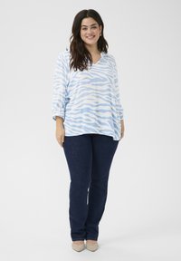 Light blue top with white zebra stripes, v-neck design, and three-quarter sleeves, paired with dark blue straight-leg jeans and beige flats.