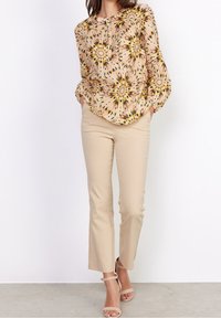 Blusa a fiori in morbido rosa, giallo e nero; presenta maniche lunghe e scollatura tonda. Abbinata a pantaloni beige a gamba dritta e tacchi.