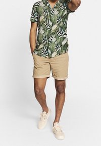 Kortærmet skjorte med grønne bladprint, kombineret med beige op rullede shorts og lyse sneakers. Simpelt, afslappet outfit.