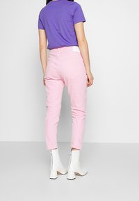 Rosa denimbyxor med smal passform, med bakfickor och en vit etikett. Matchas med en lila t-shirt och vita klackstövlar vid ankeln.