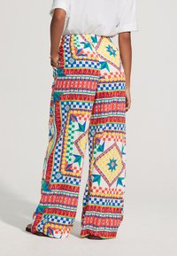 Pantalon à jambes larges en tissu coloré à motifs géométriques rouges, jaunes, bleus et verts, avec une taille haute.