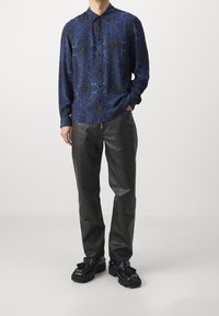 Koszula z długim rękawem w ciemnym niebieskim kolorze z wzorem damaskowym, zestawiona z czarnymi skórzanymi spodniami i błyszczącymi czarnymi butami na masywnej podeszwie z frędzlami.