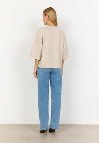 Top lavorato a maglia beige chiaro con maniche ampie, abbinato a jeans blu a vita alta. L'outfit è completato da scarpe con tacco scure.