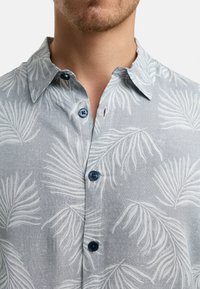 Camisa de manga corta en tela azul clara con un patrón de hojas de palma, con acentos en gris claro y botones azules oscuros en el frente.