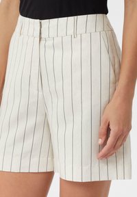 Weiße Shorts mit schmalen, vertikalen, marineblauen Streifen, die eine glatte Textur haben, Seitentaschen und einen Bund mit einem dezenten Verschluss aufweisen.