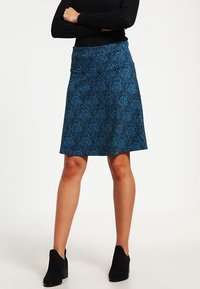 Una falda acampanada con un patrón floral azul y una textura suave. Tiene una cinturilla ajustada y cae por encima de las rodillas, combinada con botas negras hasta los tobillos.
