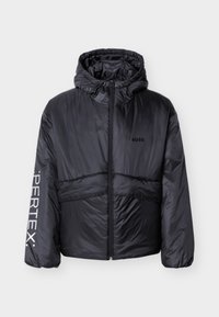 Μαύρο μπουφάν puffer με κουκούλα, φερμουάρ μπροστά, λογότυπο "HUGO" στο στήθος και κείμενο "PERTEX" στο αριστερό μανίκι, εμφανίζεται σε λευκό φόντο.