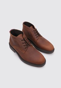 Botines de cuero marrón con textura lisa, diseño con cordones, punta redonda y suelas de goma oscuras a contraste. Detalles con costuras visibles.