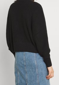 Svart, ribbat stickad tröja med en kort design och långa ärmar, ihop med en blå denimkjol med vertikala sömmar.