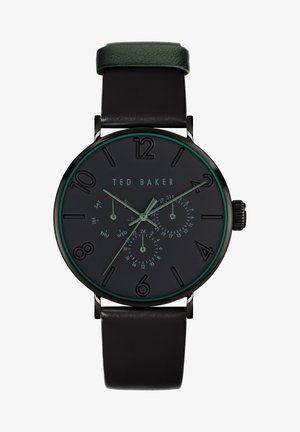 Svart analog klocka med gröna detaljer, svart urtavla, stora timmarkörer och subdials för dag och datum. Svart läderarmband.