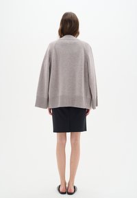 Světle šedý pletený oversized svetr s ribbeným lemem, širokými rukávy a složeným límcem, ve spojení s tmavě modrou tužkovou sukní.
