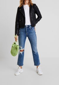 Svart läderbikerjacka, vit t-shirt, slitna blåjeans med hål, vita sneakers och en strukturerad grön virkade väska.