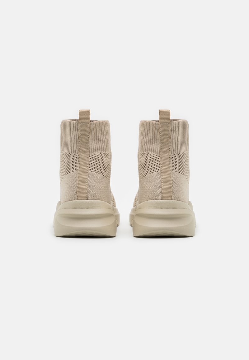 Bottines à chevilles en tricot beige avec une tige en mesh texturé, des accents élastiques tan et une semelle rembourrée pour le confort. Deux tirants à l'arrière.