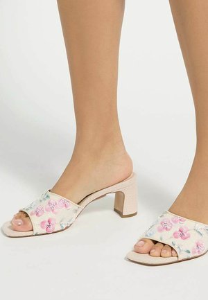 Feet wearing open-toe, cream-colored block heel sandals with pink and blue floral embroidery on the straps.