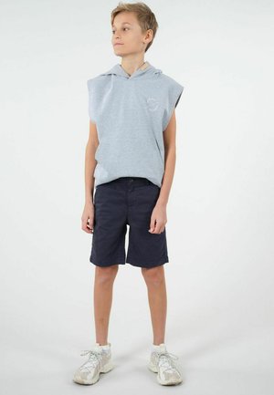 Hoodie sans manches gris avec cordon de serrage et logo, associé à un short bleu marine. Le modèle porte des baskets claires avec des lacets réfléchissants.
