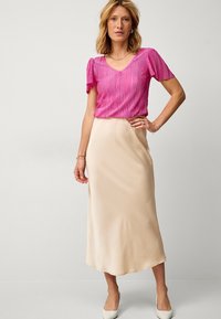 Fuchsia plisseret top med korte ærmer, parret med en beige satin midi-nederdel og lyse spidse sko; glatte teksturer, elegant silhuet.