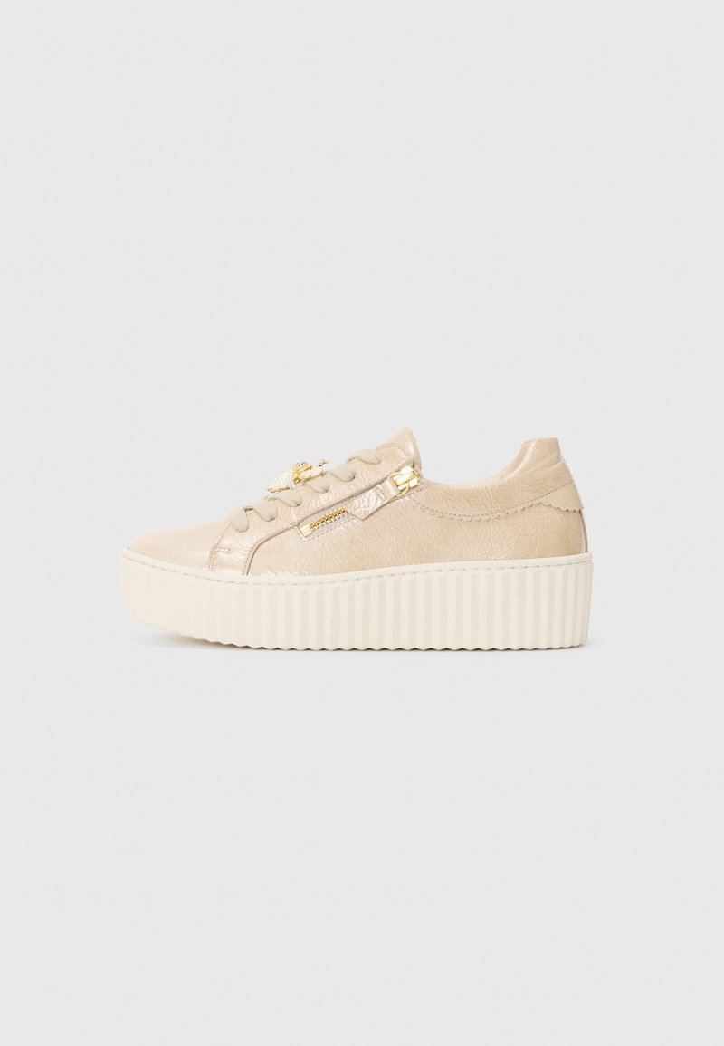 Baskets en suède beige avec une épaisse semelle plateforme crème, présentant des accents métalliques et un détail de fermeture éclair décoratif sur le côté.