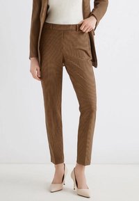 Pantaloni a quadri marroni realizzati in tessuto leggero, con vestibilità sartoriale, frontale piatto e pieghe sottili, abbinati a tacchi alti beige.